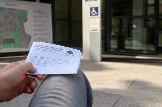 Hand holding a CERFA document in a public waiting area, with tactile map and accessibility signage softly visible in the background