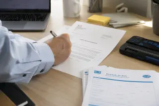 Worker's hand annotating a French dismissal document on a desk next to a Braille display and CERFA forms in soft natural office light.