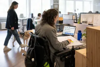 Two people at an office desk review and annotate a printed French administrative form, focus on their hands, with an accessible computer interface and calm natural daylight in a real workspace.